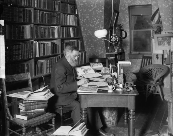 Rasmus B. Anderson seated in his study and taking notes from a book.