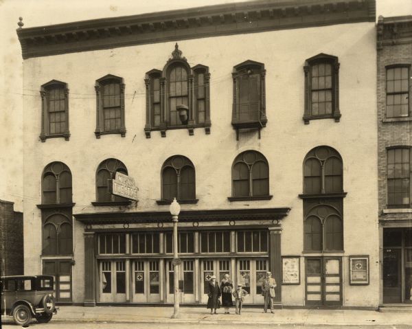 Exterior view of Wilson Theater. Standing on sidewalk from left to right are: Delia Berry Wilson, Orpha Wilson, Robert Paul Hollis, and Robert Henry Wilson. Wilson Theater, also known as Wilson Opera House, was originally named Goodwin House (dedicated as such on December 27, 1869). The Building later became The Beloit Bank. The Wilson family lived at 605 St. Lawrence Avenue and was occupied by the family until 1974.

