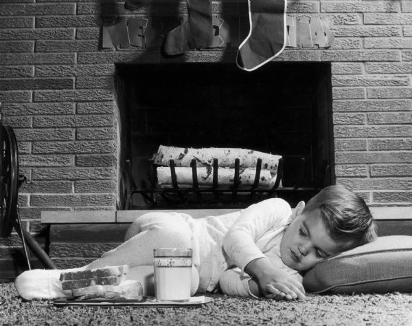 Child sleeping in front of the fireplace, waiting for Santa Claus to arrive.