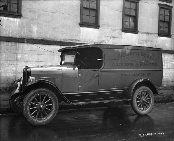 International truck operated by Barsotti Brothers, Grocers and Bakers. The truck is parked on a wet city street.