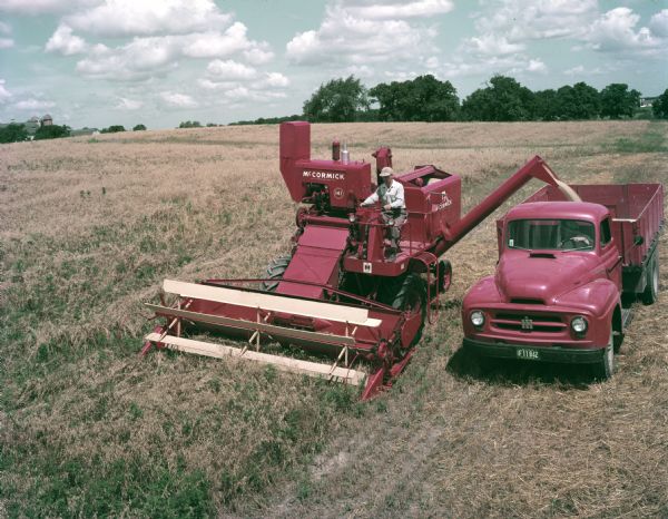 Color photograph of a farmer harvesting grain with a McCormick No. 141 harvester-thresher (combine) and an International truck.