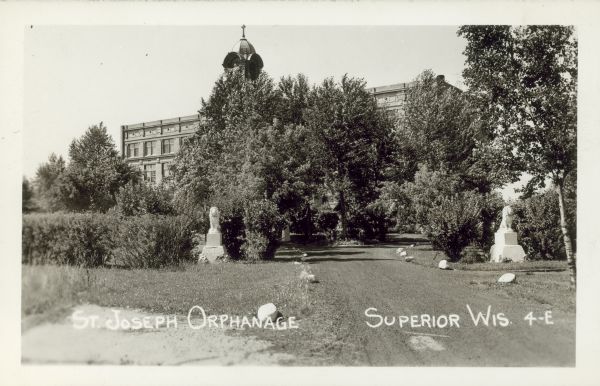 Exterior view of the St. Joseph Orphanage, with lion statues at the entrance. Caption reads: "St. Joseph Orphanage, Superior, Wis."