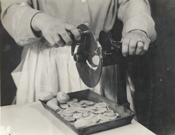 Close-up of a woman's hands using a potato slicer attached to a counter.