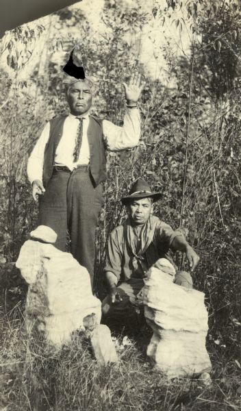 Two Native American men, one of whom is holding his hand palm up, pose with two piles of spirit stones.