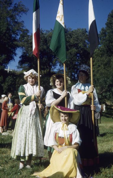 Four women in Swiss costume, three of whom are holding flags, at the Wilhelm Tell Festival.