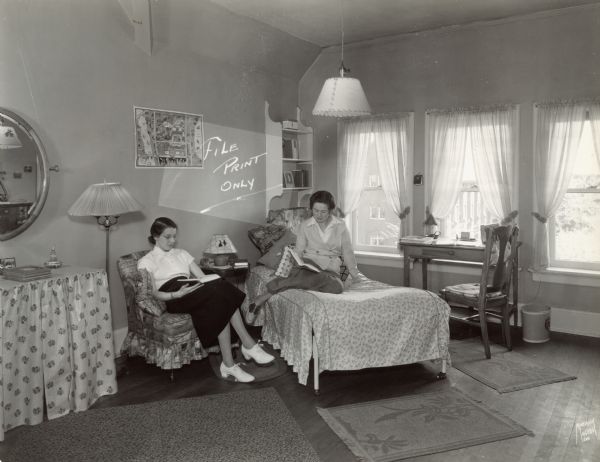 Two women casually reading in a dorm room at Milwaukee-Downer College. A map of Milwaukee hangs on one wall.