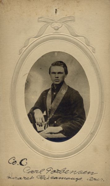 A seated studio portrait of Carl Tjorbjornsen [as written on the photograph backing and Descriptive Rolls, Volume 20; also written as Carl Torbjorson published roster: Wisconsin Volunteers (1914); also as Carl Torbjornsen  on published roster: Rosters of Wisconsin Volunteers, Volume 1 (1886)], a corporal in Company C, 15th Wisconsin Infantry, in uniform.  The following information was obtained from the Regimental and Descriptive Rolls, Volume 20: He resided in Muskego, Wisconsin.  On November 28, 1861, he enlisted in Madison, Wisconsin and on December 12, 1861 he was mustered into service in Madison, Wisconsin at the age of 20. He was wounded on September 19, 1863 during the battle at Chickamauga, Georgia.  Following the battle, he was sent to a hospital where he spent the remainder of the war recovering from his wounds. He mustered out with Company C on December 31, 1864, at Chattanooga, Tennessee.