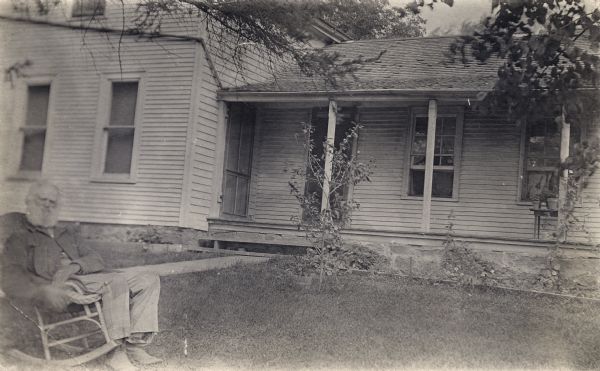 Anson Case seated in a rocking chair in front of his home.