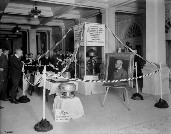 Exhibition about the contributions of Stephen M. Babcock to the history of the dairy industry in the lobby of the State Historical Society Building. Both the original and a new motorized butterfat tester are on display. The photograph may depict the formal opening of the exhibit.
