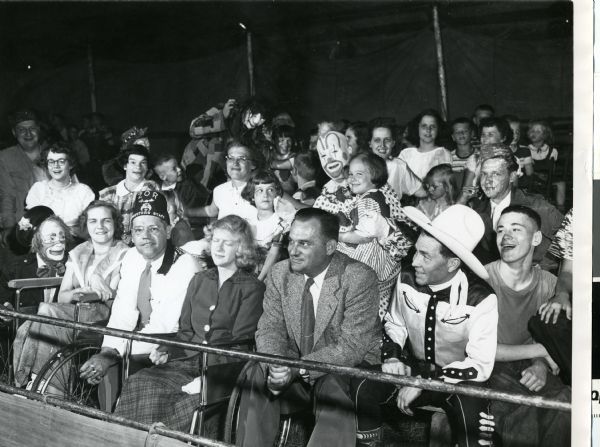 Madison Mayor, George Forrester, seated in the front row of the audience at the Ringling Brothers Circus. Clowns entertain the children seated near Forrester. A Shriner sits in the first row.