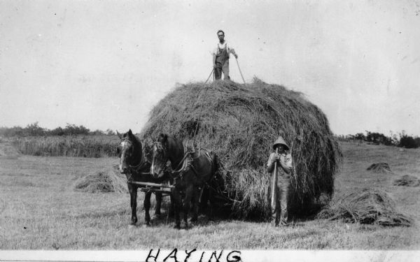 Several farmers posing with a very large haystack. A man identified as "Uncle Dave" is standing on top of the hay.
