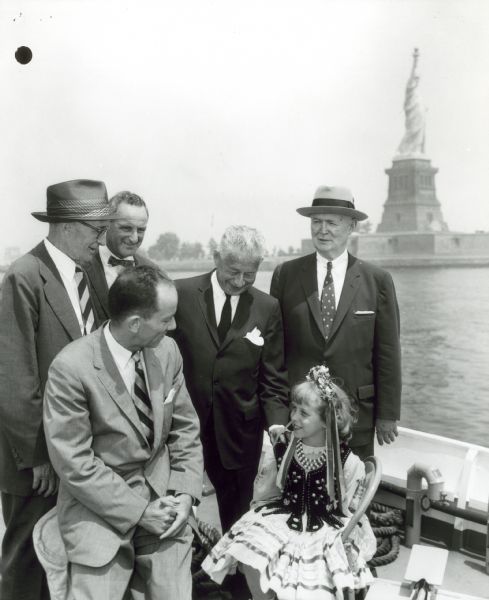 Arthur W. Page (far left in eyeglasses and hat), poses with business associates and a little girl in costume. The Statue of Liberty is in the background.