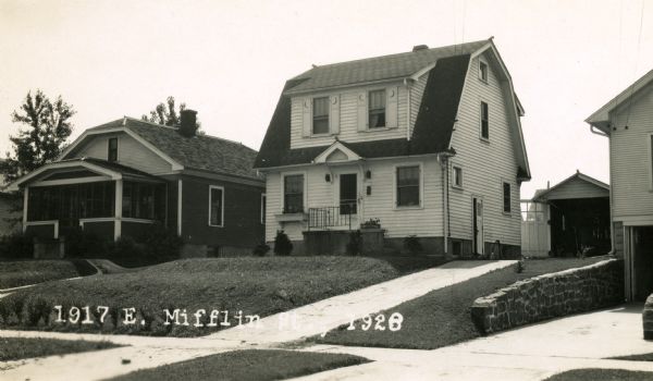 Exterior of the house at 1917 East Mifflin Street, built by Willard Droster. The garage behind the home can be seen as well as the house at 1919 East Mifflin street. There is a retaining wall along the neighboring driveway on the right.