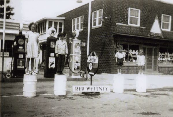 Children standing on barrels in front of Droster Grocery and Filling Station at 1438 Sherman Avenue, run by Red Whitney. The children are Whitney's nieces and nephews.