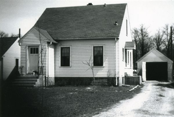 Exterior of the house at 1705 Sheridan Drive and the garage behind it shortly after construction. The house was built by Willard Droster.  There is a dog on the porch.