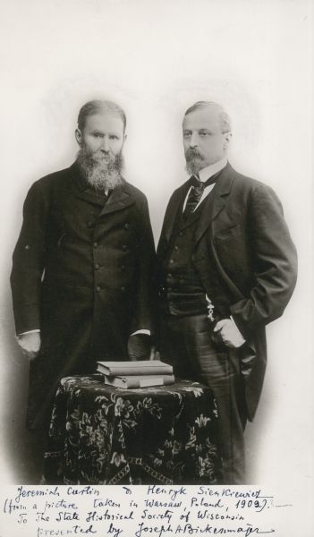 Jeremiah Curtin and Henryk Sienkiewicz standing in front of a table with books on it.
