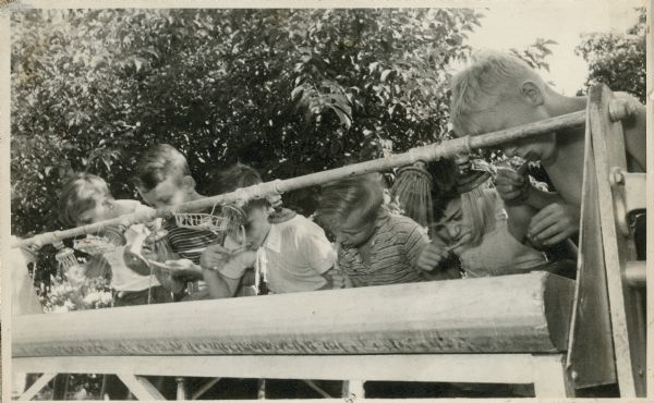 A row of children brush their teeth outdoors at camp.