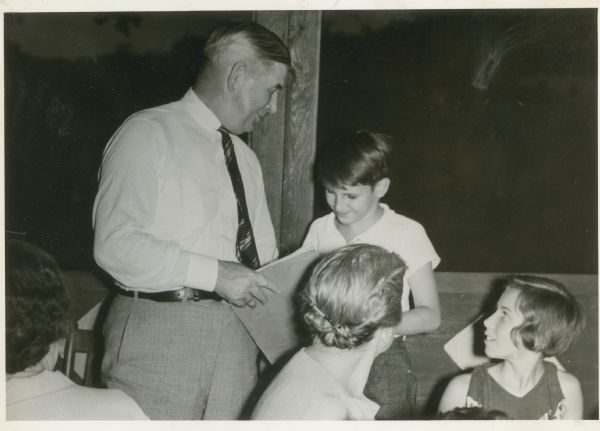 A smiling boy hands a scrapbook to William T. Evjue as a girl and woman look on.