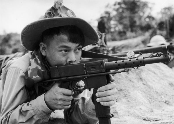 Propaganda photograph received by the National Coordinating Committee Against the War in Vietnam for use in its newsletter. This photograph was produced by an unidentified official source. It is captioned: "With the South Vietnam Liberation Armed Forces are many boys like this one, who uses a sub-machine captured in battle."