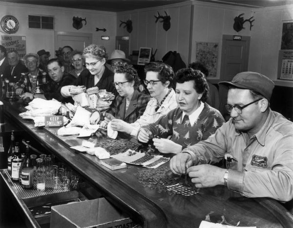 People counting pennies that came in the mail for the Dr. Kate Million Penny fundraiser.
Country doctor Kate Pelham Newcomb -- known as "the angel on snowshoes" for her willingness to go wherever she was needed during harsh northern winters -- spearheaded a movement in 1953 to build a much-needed hospital in Woodruff, encouraging local children to collect a million pennies. The effort captured everyone's imagination, and coins came in the mail from every state and many foreign nations. Her dream came true in 1954 when the Lakeland Memorial Hospital opened its doors.<br>A giant penny was created to commemorate this event, and "The World's Largest Penny" still sits in the city park of this picturesque northern Wisconsin town.<br>In 2003, the community celebrated the 50th anniversary of the first Million Penny Parade, with a parade featuring those who participated in the original parade and "Dr. Kate Babies" - those who had been delivered by Dr. Newcomb. The hospital is now the Howard Young Medical Center (which they proudly proclaim started with "just one penny"), and in 1988 the community created the Dr. Kate Newcomb Museum.<p>The WHS Press has published a children's book on her life called "Dr. Kate: Angel on Snowshoes."</p>