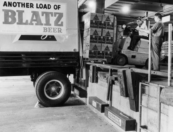 Two men using a fork lift to load cases of beer into a truck at the Blatz brewery. The two men are Edward Klem, guiding the fork lift truck, and Frank Le Bouton.