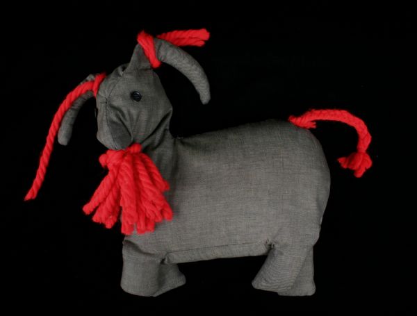 A stuffed toy goat with a gray body and a red tail, beard and ears.