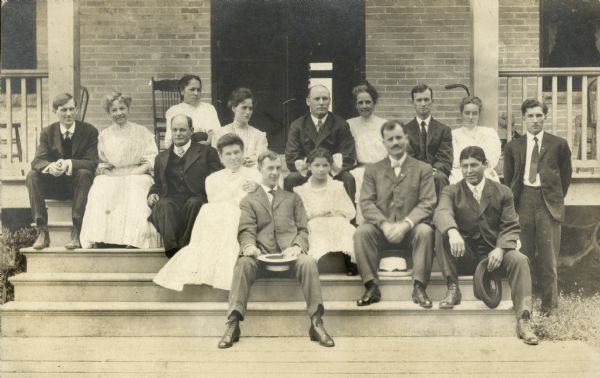 Group portrait of eight men and seven women on the steps of the Keshena Boardinghouse.