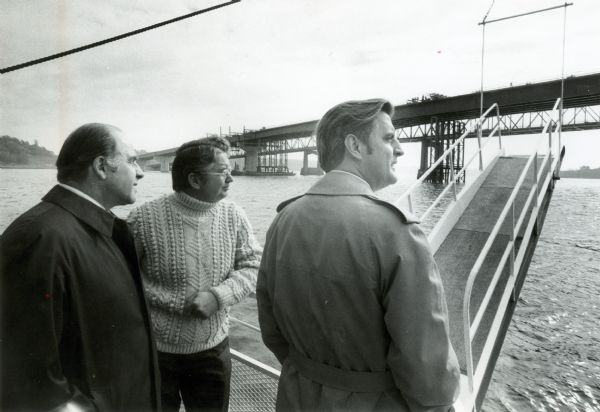 Gaylord Nelson, Patrick Lucey, and Walter Mondale look over the St. Croix River. In the background a bridge is under construction.