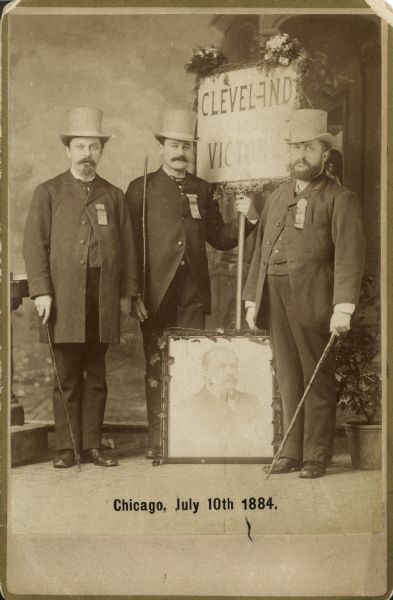 Three men in matching hats pose with a photograph and a sign in support of Grover Cleveland.