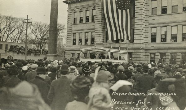 Postcard of large group watching as Mayor Abrams introduces President Taft. Caption reads: "Mayor Abrams introducing President Taft, Green Bay, Wis."