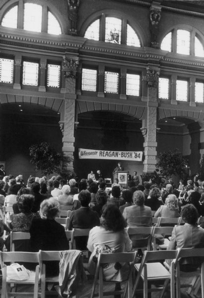 An unidentified speaker addresses a crowd beneath a banner that reads "Wisconsin Reagan-Bush '84".