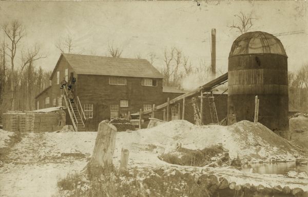Exterior view of the shingle mill near Mellen, with five men, probably employees, posing on and near the outdoor stairway of a building. From bottom to top are Christian Hanson, Arnold Becker, George McLeod, Charles Carroll (right) and Mose Mayfield (left).