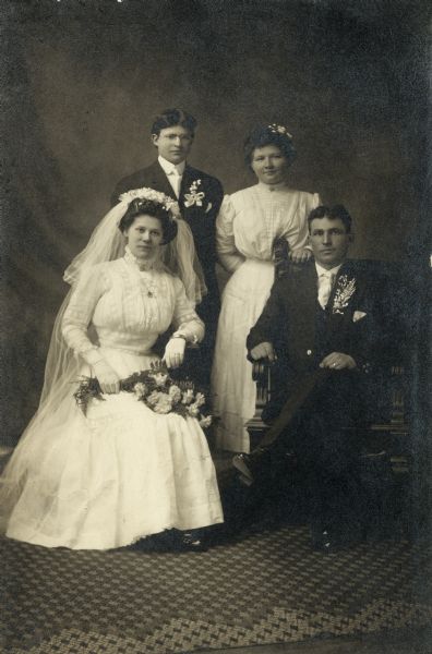 Studio group portrait of Rose and Louis Meyer's wedding party. Rose Swetlik (1892-1968) married Louis Meyer (1887-1949), a farmer, on February 28, 1911 in Kossuth Township (Manitowoc Co.), WI. The wedding party then drove to Manitowoc to have their photographs taken. Bride and groom are seated in front; best man Victor Meyer (groom's brother) and maid of honor Ella Popelars (bride's cousin) stand at the back. Wedding party dressed in formal wedding attire.