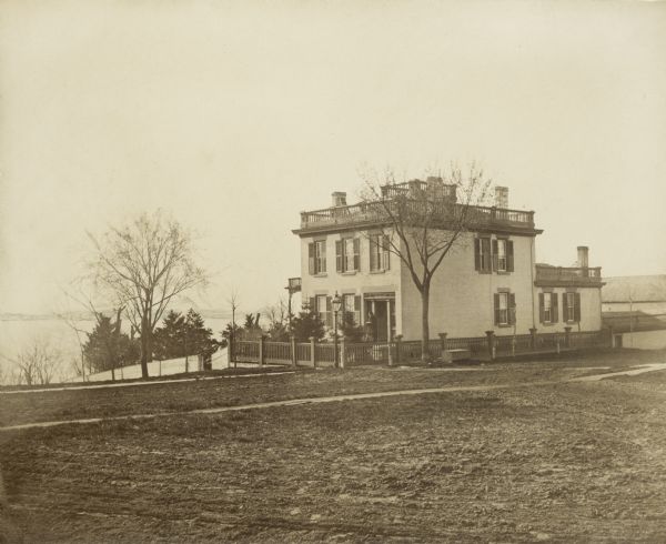 Early view of the house built by Madison's first mayor, Jairus C. Fairchild, at 302 South Wisconsin Avenue (renamed Monona Avenue in 1877) at West Wilson St. near Lake Monona. There is a woman standing near the front door. The house was constructed in 1850 and later was substantially altered with additions. After the Civil War, the house became the home of Fairchild's son, Lucius, Civil War hero, Wisconsin governor (1866-72) and foreign diplomat. During his six years as governor, the Fairchild House was the state's executive residence, as no such property was then owned by the state. The residence was therefore a focus of Madison's political and social life during the last half of the 19th century.
