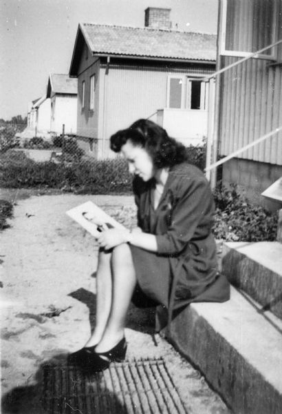 Portrait of Pela Rosen Alpert in Kristianstad, Sweden. She is sitting on the steps outside of a house looking at a photograph.