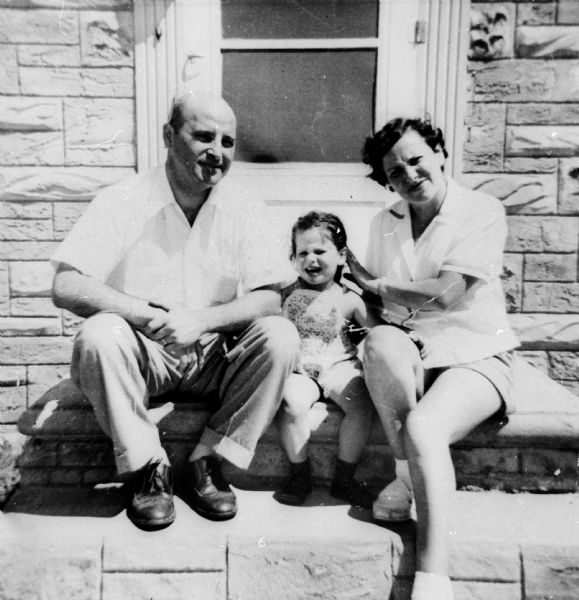 Pela Rosen Alpert, Richard Alpert, and daughter Rochelle seated outside on front steps of house.