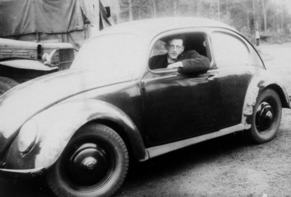 Fred Platner driving a Volkswagen for the American Jewish Joint Distribution Committee; Bergen Belsen, Germany.