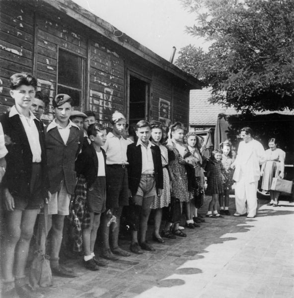 Refugee children stand in line as they wait to go on an outing; Munich.

Saul Sorrin was interviewed as part of the Wisconsin Survivors of the Holocaust Interviews project. Sorrin, born in New York in 1919, applied in 1940 for a position with the United Nations Relief and Rehabilitation Administration (UNRRA). He worked with Holocaust survivors as a supply officer for UNRAA team 560 at the Displaced Persons camp Neu Freimann Siedlung in Germany and later, at General Dwight D. Eisenhower's recommendation, Sorrin became the Area Director of the International Refugee Organization based at the Wolfratshausen DP camp in Bad Kissingen.

When asked about this image, Sorrin revealed, "This is again children.  This slips me.  I imagine this is outside of some warehouse in one of the DP camps in Munich and the children may have been going on an outing or they may have been going on some sort of a youth group function."

Interview by Jean Loeb Lettofsky and David Mandel, March 3, 1980.