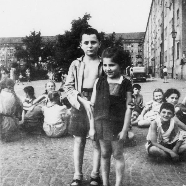 Jewish orphans between takes while appearing in Fred Zinneman's film, "The Search"; Germany.

Saul Sorrin was interviewed as part of the Wisconsin Survivors of the Holocaust Interviews project. Sorrin, born in New York in 1919, applied in 1940 for a position with the United Nations Relief and Rehabilitation Administration (UNRRA). He worked with Holocaust survivors as a supply officer for UNRAA team 560 at the Displaced Persons camp Neu Freimann Siedlung in Germany and later, at General Dwight D. Eisenhower's recommendation, Sorrin became the Area Director of the International Refugee Organization based at the Wolfratshausen DP camp in Bad Kissingen.

Part of Sorrin's interview includes Sorrin speaking about the photos he took while serving for the International Refugee Organization and the UNRRA.

When asked about this image, Sorrin revealed "Yes, I know what this is.  These are Jewish children who are orphans and who were in an orphan home.  Some of the children whom we have found who are now in Israel someplace.  Now they were taken by a movie company.  I think I mentioned this to you.  Fred Zinnemann was the director of a motion picture called "The Search".  It dealt with the story of a woman, she was not Jewish, who during the war was separated from her child and after the war began the business of searching for him.  The child is in the meantime found in the wreckage of the immediate postwar period by Montgomery Clift acting as an America soldier.  He takes the child, there's a period where the child is not trustful of anybody and portrays that, and then he wins the trust.  Then the woman somehow or other finds the child.  

I remember she was a Czech opera star who played this role.  And there was an American actress who played the role of a UNRRA worker.  I remember she wore the patch, UNRRA.  Aline MacMahon.  I don't know whether you remember that actress but she was a fine actress.  Despite her name, she was Jewish.  She was married to Horace MacMahon, a famous actor. 

They used the children to play the role.  These children are dressed in the costumes as they saw them as refugee waifs, childless waifs, and they are in between takes.  They were sitting on the ground in this Kaserne,  in this building, and they're in between movie takes.  Zinnemann directed "High Noon".  He's still directing.  He's an Austrian.  And we supplied them with the children.  They gave each child candy and cookies and each child got a watch as a gift which was a tremendous thing for those children.  They were very good.  They were supposed to run someplace and shout with glee and then he took another take.  He wasn't quite sure of that.  They did it over and over again.  This picture shows the children sitting on the ground between the takes.  

I lent them a lot of gasoline out of our stores, you know, for their trucks and their cars.  I lent them some other things that they could use and I did it unofficially but we never got it back.  I pursued them.  I said, 'Where's my gas?  Where's my this, that?'  And they left.  But we were proud about our role in the making of this movie, which I think was shown here about 1948."

Interview by Jean Loeb Lettofsky and David Mandel, March 3, 1980.

