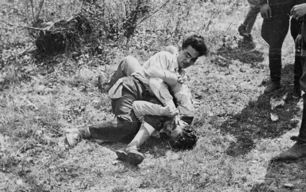 Refugees "horsing around" on the ground.

Saul Sorrin was interviewed as part of the Wisconsin Survivors of the Holocaust Interviews project. Sorrin, born in New York in 1919, applied in 1940 for a position with the United Nations Relief and Rehabilitation Administration (UNRRA). He worked with Holocaust survivors as a supply officer for UNRAA team 560 at the Displaced Persons camp Neu Freimann Siedlung in Germany and later, at General Dwight D. Eisenhower's recommendation, Sorrin became the Area Director of the International Refugee Organization based at the Wolfratshausen DP camp in Bad Kissingen.

When asked about this image, Sorrin revealed, "No, no, that's simply horsing around. Two young fellows. There was a great macho thing among the Jews. One day a guy  came into the camp, I saw him. He was absolutely the duplicate of an SS man in his suit, boots, hat. He just ripped all the buttons and the insignia off. They stole or took from wherever they could get, from fleeing German military. They took their boots. They wore those boots, shtivl. They wore German, and many of them wore Russian equipment because they had served in the Russian army and the Russian military in the beginning. And the girls wore boots. I think I told you. They looked very attractive as boots do today. I've thought about it because boots were unknown to me--in the United States in the 1930s when I was growing up a girl didn't wear boots. Then I saw these women come in with their boots and they looked--there's something about boots on a woman which is so sensuous. Do you agree?  Well I saw for the first time these girls these girls who really had nothing but themselves. I mean if they made it through the war some of them--I think I mentioned to you I think the Hungarians were always just terrific."

Interview by Jean Loeb Lettofsky and David Mandel, March 3, 1980.
