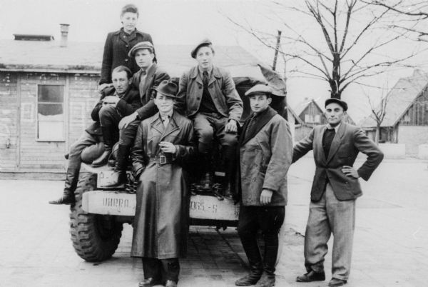 Displaced persons camp ambulance drivers standing on a UNRRA (United Nations Relief and Rehabilitation Administration) jeep.  The man in the front, center, was a partisan during WWII; Germany.

Saul Sorrin was interviewed as part of the Wisconsin Survivors of the Holocaust Interviews project. Sorrin, born in New York in 1919, applied in 1940 for a position with the United Nations Relief and Rehabilitation Administration (UNRRA). He worked with Holocaust survivors as a supply officer for UNRAA team 560 at the Displaced Persons camp Neu Freimann Siedlung in Germany and later, at General Dwight D. Eisenhower's recommendation, Sorrin became the Area Director of the International Refugee Organization based at the Wolfratshausen DP camp in Bad Kissingen.

When asked about this image, Sorrin revealed, "I think these fellows were our ambulance drivers, posing as a group. We had a very big population. People got sick. They drove ambulances but they also drove other vehicles. I remember this young man in his leather coat up front, and I wonder where this guy is. He was a young guy who'd seen it all. I remember him very clearly. He'd been a partisan. You can just tell by the tilt of that hat, you know, and the way he's standing there. He had a real sense of bravado. He used to say, 'Khaver Direktor, I could do anything.' He went out and got that leather coat some place in Germany. You can just tell, looking at him compared to the others that he--I don't remember his name, but these are a group of drivers in the motor pool of one of the DP camps."

Interview by Jean Loeb Lettofsky and David Mandel, March 3, 1980.