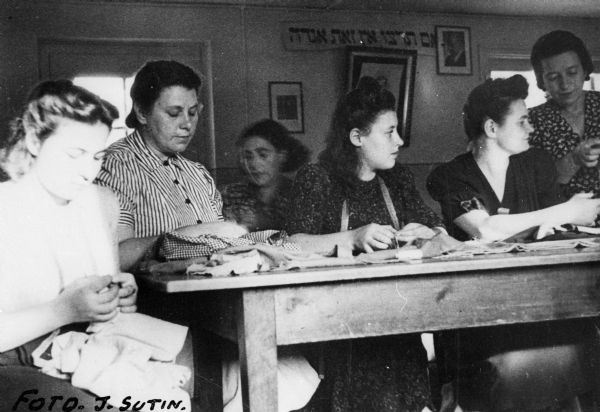 Women learning the dressmaking trade at an ORT school in a displaced persons camp; Germany.

Saul Sorrin was interviewed as part of the Wisconsin Survivors of the Holocaust Interviews project. Sorrin, born in New York in 1919, applied in 1940 for a position with the United Nations Relief and Rehabilitation Administration (UNRRA). He worked with Holocaust survivors as a supply officer for UNRAA team 560 at the Displaced Persons camp Neu Freimann Siedlung in Germany and later, at General Dwight D. Eisenhower's recommendation, Sorrin became the Area Director of the International Refugee Organization based at the Wolfratshausen DP camp in Bad Kissingen.

When asked about this image, Sorrin revealed, "This is an ORT school.  Can't see what it says in the back. These ladies are learning dressmaking. We had the ORT schools and they taught a variety of trades--dressmaking, clothing cutting, watchmaking, shoemaking, shleser, that was mechanics. A shleser is a machinist. We had carpenters, and all of the rest of these trades. The people wanted to learn and they did learn. And they were paid to learn. Not in dollars, not in money or marks, but in extra rations. So we had quite a ?. And you could get into two or three courses, you could get two, three rations. "

Interview by Jean Loeb Lettofsky and David Mandel, March 3, 1980.
