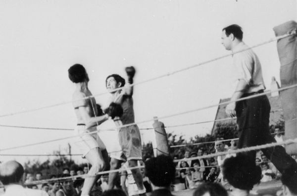Boxing match, most likely between refugees, at a displaced persons camp; Germany. 

Saul Sorrin was interviewed as part of the Wisconsin Survivors of the Holocaust Interviews project. Sorrin, born in New York in 1919, applied in 1940 for a position with the United Nations Relief and Rehabilitation Administration (UNRRA). He worked with Holocaust survivors as a supply officer for UNRAA team 560 at the Displaced Persons camp Neu Freimann Siedlung in Germany and later, at General Dwight D. Eisenhower's recommendation, Sorrin became the Area Director of the International Refugee Organization based at the Wolfratshausen DP camp in Bad Kissingen.

When asked about this image, Sorrin revealed, "Boxing matches. I told you before that we loved boxing. I was asked in this occasion to referee a--I think they were the opening matches. Asked me if if I'd get up there and referee. I refereed four or five boxing matches.  We erected the ring around the middle of one of the camps. They were not very skillful but they had a lot of enthusiasm. As I told you, we boxed a team match against the 3rd Army boxing team and we beat one or two or three of those fellows. One at least I remember was ETO boxing, European Theater boxing champion."

Interview by Jean Loeb Lettofsky and David Mandel, March 3, 1980.