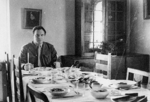 Self-portrait of Saul Sorrin, area director of the International Refugee Organization, dining at his former house in Munich.

Saul Sorrin was interviewed as part of the Wisconsin Survivors of the Holocaust Interviews project. Sorrin, born in New York in 1919, applied in 1940 for a position with the United Nations Relief and Rehabilitation Administration (UNRRA). He worked with Holocaust survivors as a supply officer for UNRAA team 560 at the Displaced Persons camp Neu Freimann Siedlung in Germany and later, at General Dwight D. Eisenhower's recommendation, Sorrin became the Area Director of the International Refugee Organization based at the Wolfratshausen DP camp in Bad Kissingen.

When asked about this image, Sorrin revealed, "Since I'd become a first-rate trencherman, I decided to pose this picture at the head of the table in our staff mess in my house. This is on the Klementinenstrasse by the Englischgarten in Munich. This is a house which had been taken from a high-ranking Nazi by the name of Von Schrerien. He has been the finance minister of Bavaria. We had about a dozen people or eight people who came to our mess every day, whenever it was possible. It was probably a dinner hour. I see we got the plates out here. We had a staff including a Jewish cook, the cousin of a friend of mine, a survivor from Vilna and she made us all kosher-style foods. There was kosher food available for the Jewish survivors who were kosher. And she made chicken and fish and whatever and cholnt and all those good dishes. I think from the time she came, really, I'm serious, in about six months I must have picked up about twenty pounds. In this picture I'm still fairly slender. I look very much like my son, Leonard, on this picture. You haven't ever seen my son.  Just unbelievable. He's now twenty-six, exactly my age then, about twenty six."

Interview by Jean Loeb Lettofsky and David Mandel, March 3, 1980.
