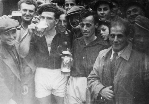 Refugees at a Displaced Persons camp celebrate a soccer victory over another D.P. camp team; Germany.

Saul Sorrin was interviewed as part of the Wisconsin Survivors of the Holocaust Interviews project. Sorrin, born in New York in 1919, applied in 1940 for a position with the United Nations Relief and Rehabilitation Administration (UNRRA). He worked with Holocaust survivors as a supply officer for UNRAA team 560 at the Displaced Persons camp Neu Freimann Siedlung in Germany and later, at General Dwight D. Eisenhower's recommendation, Sorrin became the Area Director of the International Refugee Organization based at the Wolfratshausen DP camp in Bad Kissingen.

When asked about this image, Sorrin revealed, "A victory toast. We had football players, we had a league among the Jewish DP camps. Soccer was very, very popular. They played with great enthusiasm. Hundreds, thousands of people came out to watch and then after the players would repair to the nearest invalidn bar and toast their victory.  Great spirit. But look at these faces. Here's a man in the middle there with a toothache or something, he's got a thing around his--the Jews had awfully bad teeth, terrible. We set up clinics, you know for the JDC. We had our own clinics then we set up JDC clinics."

Interview by Jean Loeb Lettofsky and David Mandel, March 3, 1980.
