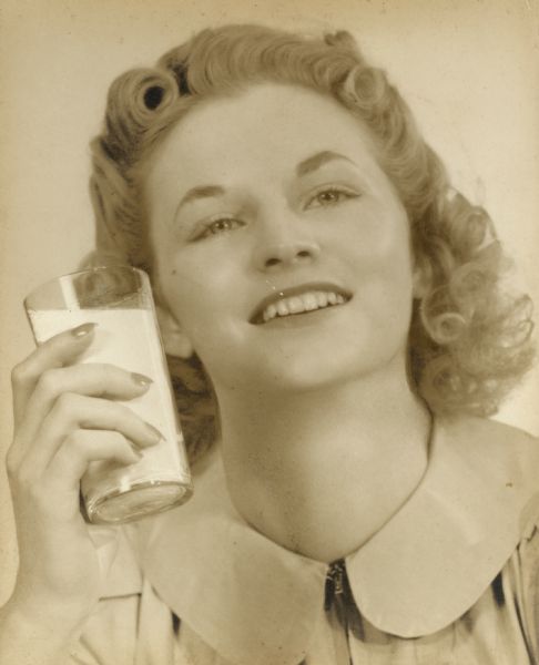 Studio portrait of Iva Kearney of Ithaca, Wisconsin, holding a glass of milk in her hand.