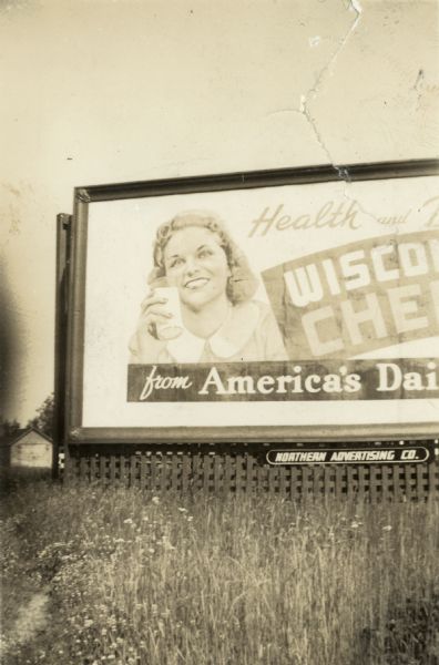 Outdoor advertising billboard rendered from a photograph of Iva Kearney of Ithaca, Wisconsin, holding a glass of milk in her hand.
