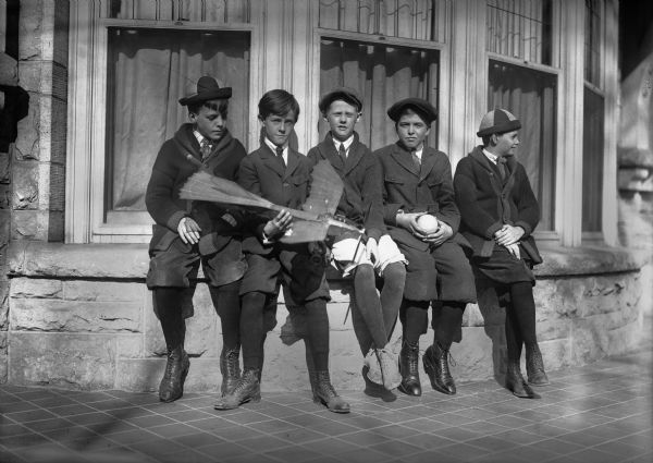 Reginald Jackson, Jr., of Madison, holding the toy airplane, and a group of friends, all of whom are wearing short pants, sitting on the windowsill in front of the Jackson home, 415 N. Carroll St.  Jackson became a physician but maintained a life-long interest in aviation, eventually heading the Wisconsin Wing of the Civil Air Patrol.