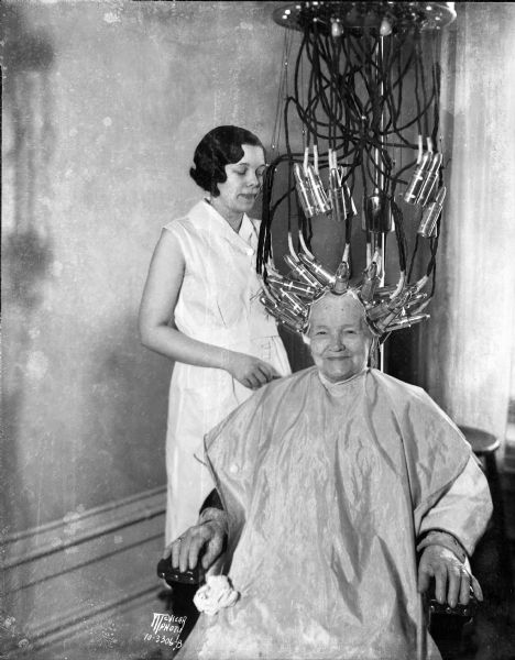 Mrs. Betsy Johnson (84-years-old) getting a permanent wave in the Elite Beauty Shop, 27 East Main Street, from her granddaughter Pearl Holman.