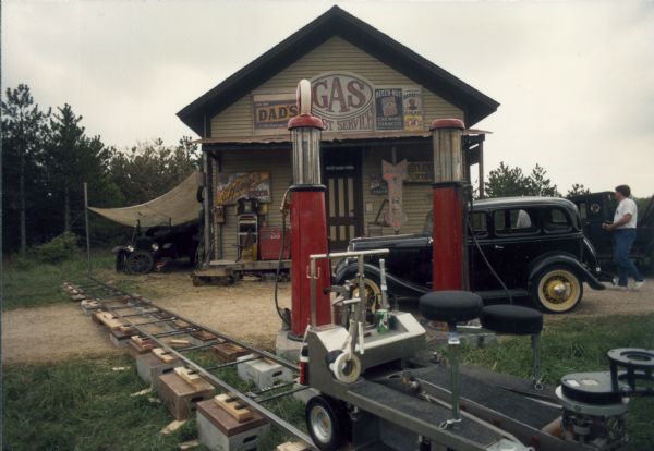 The historic Harmony Town Hall at Old World Wisconsin transformed for use as a 1930s gasoline station for the made-for-TV movie, "Dillinger." In the foreground is a car on tracks for a camera and camera operator.